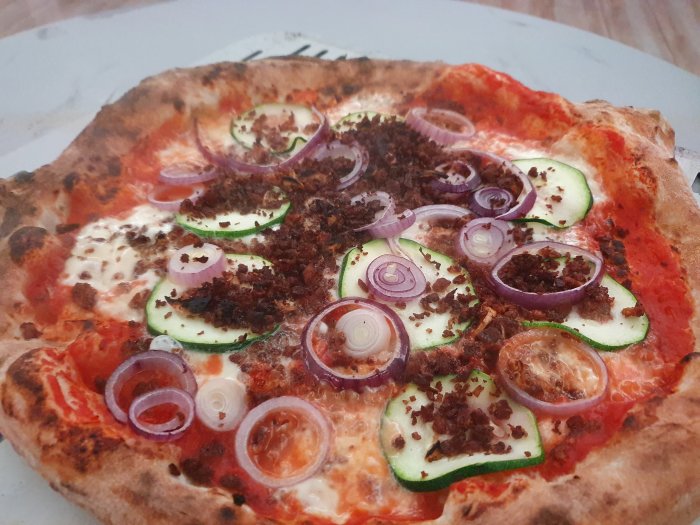 Närbild på en pizza med tomatsås, ost, köttfärs, rödlök och zucchini skivor.