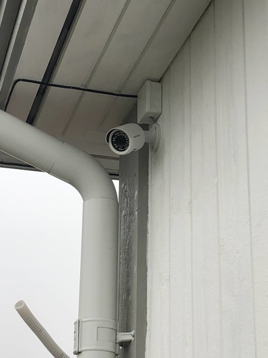 Övervakningskamera installerad på husvägg bredvid stuprör och takutsprång.