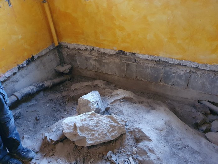 Renoveringsarbete med utgrävning i ett rum, synliga vattenrör och betongblock på golvet.