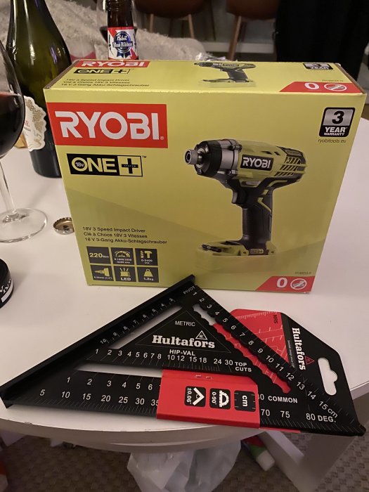 Ryobi slagskruvdragare i förpackning och Hultafors snabbvinkel på ett bord med vinflaskor i bakgrunden.