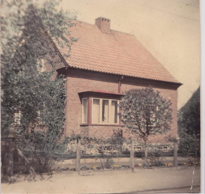 Gammal fotografi av en tegelhusfasad från 50-talet med ett rött tegeltak, vita fönsterkarmar och en liten trädgård.
