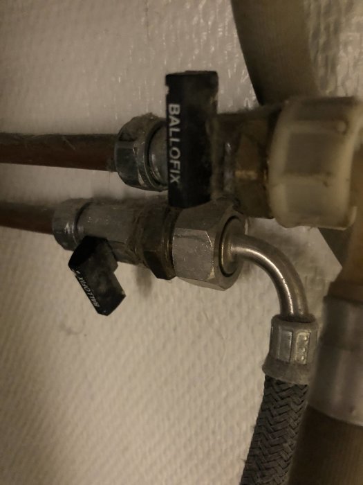 Rörkopplingar under ett handfat med stängda ballofixventiler för varmt och kallt vatten.
