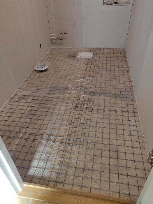 Armeringsnät utlagt på golv i förberedelse för flytspackling, med synliga kakelkryss och avlopp.