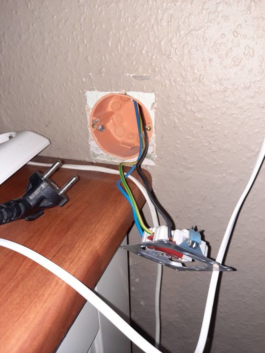 Öppet eluttag med kablar under byte, moderna exxact med petskydd installerat, vägg med tapet.