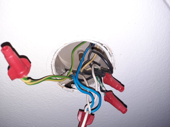 Öppet vägguttag med exponerade elkablar och säkerhetsklämmor i en rörinstallation.