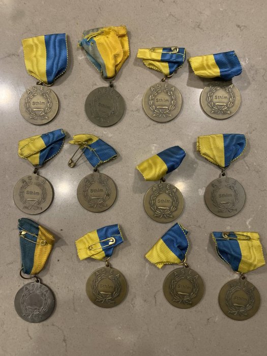 Samling medaljer med texten "ASEA Sthlm" och blågula band på en marmorbänk.