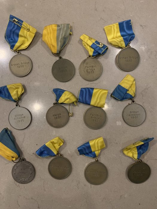 Gamla metallmedaljer med blå och gula band från 1950- och 1960-talen på en ljus yta.