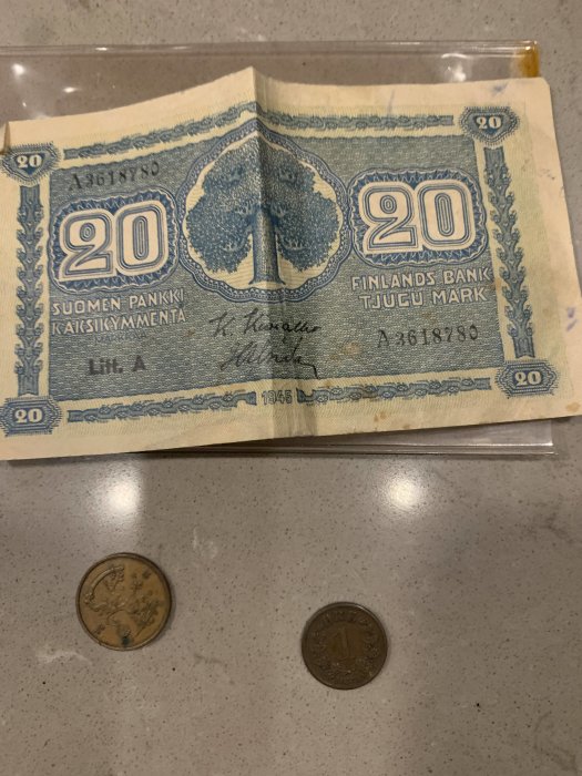 Ett gammalt 20 finska mark-sedel från 1945 och två mynt på en bordsyta.