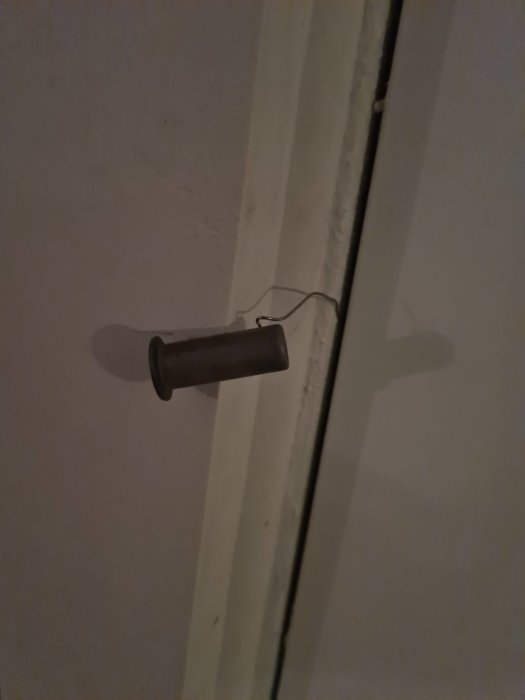Givare till golvvärme utan låda, hängande på en vit vägg med synlig tråd.