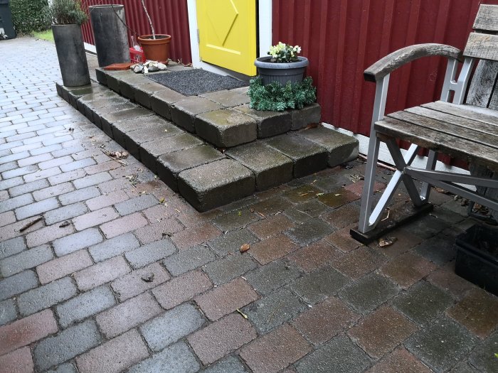 Stapelade betongblock som bildar en trappa utanför en entrédörr, med en gammal träbänk intill.