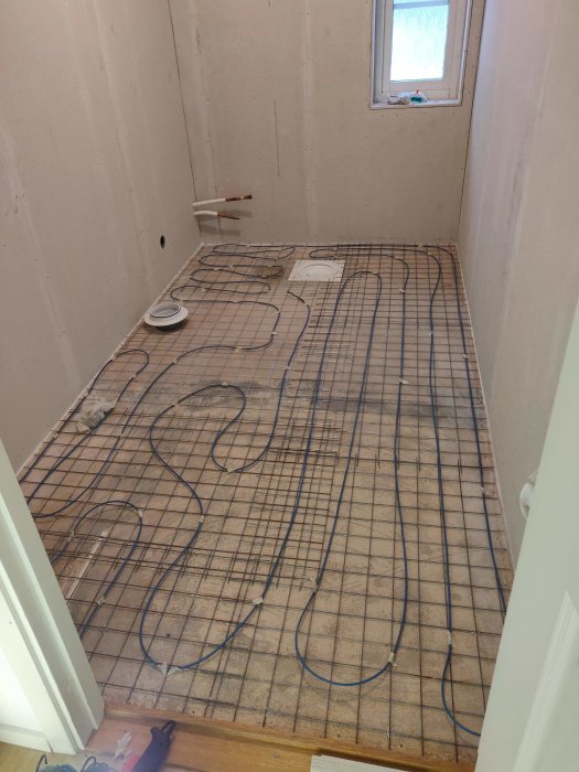 Golvvärmekabel temporärt utlagd på golvet för komfortvärme i ett tomt rum med fibrerarmeringsnät.