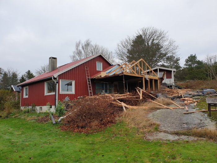 Rött hus med påbörjad rivning av ett sadeltak och byggavfall spridd runtomkring.