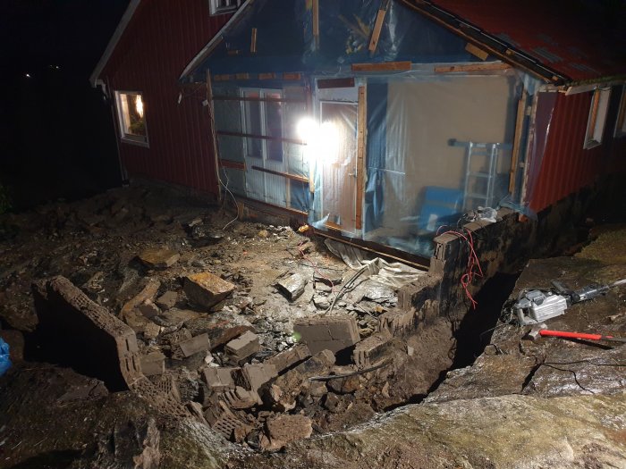 Rivning av grundmur vid ett hus i nattbelysning, med högar av tegelsten och byggbråte.