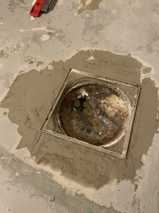 Renoverat badrumsgolv med påbörjat tätskiktsarbete och en gammal avloppsbrunn.