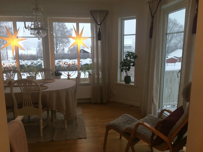 Matplats med bord och stolar, snöutsikt genom fönster, adventsstjärnor och kristallkrona.