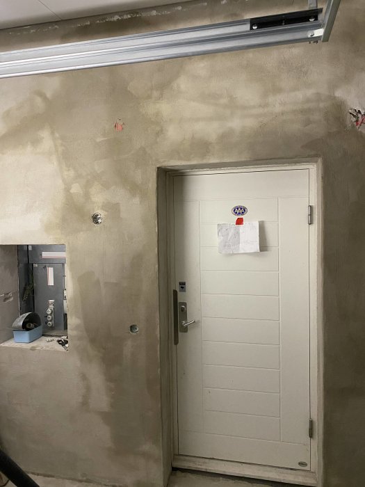 Nyligen putsad vägg i garage med vit dörr, elpanel och skenor för garageport.