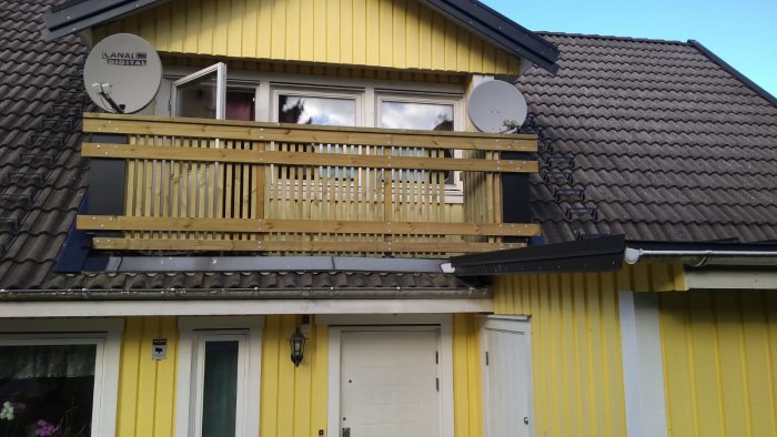 Nyrenoverad balkong med träribbor och paneler på ett gult hus med tegeltak.