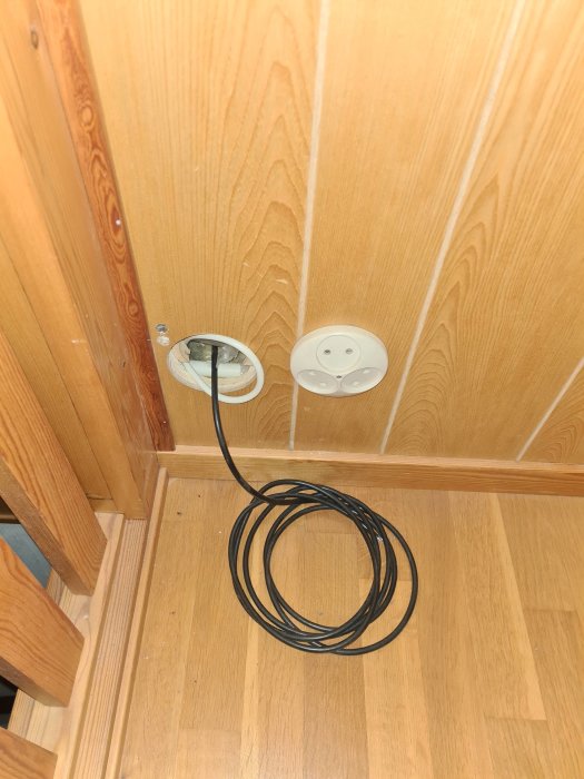 Kabel dragen genom hål i vägg med närliggande eluttag, misstänkt skadat radiatorrör bakom.