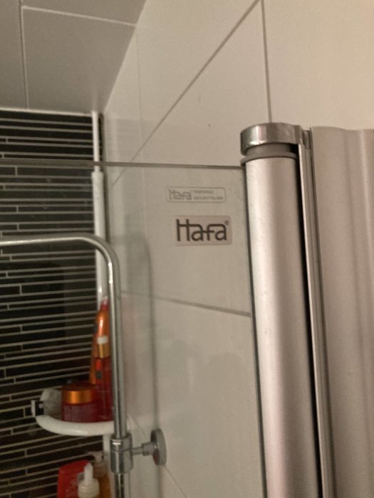 Hafa-duschvägg i ett badrum med synlig logotyp, duschstång och några badrumsprodukter.