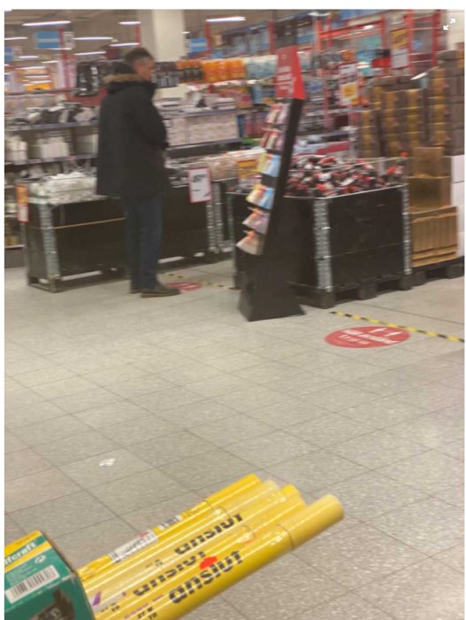 Person som handlar i en butik, håller avstånd med tydliga markeringar på golvet.