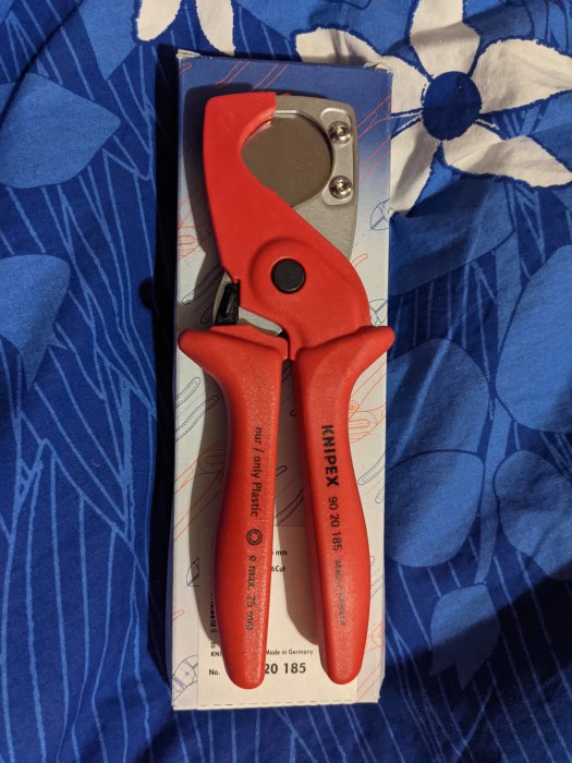 Röda Knipex avbitartång ligger på ett blåvitt mönstrat tyg ovanpå sin förpackning.