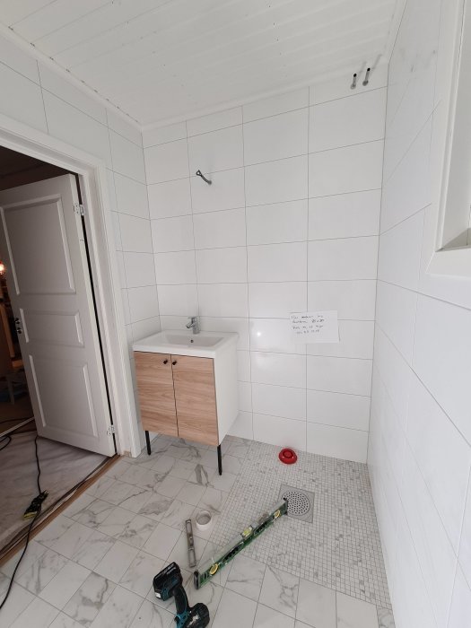 Renovering av badrum med vita väggkakel, marmormönstrat golv och nya sanitetsinstallationer.