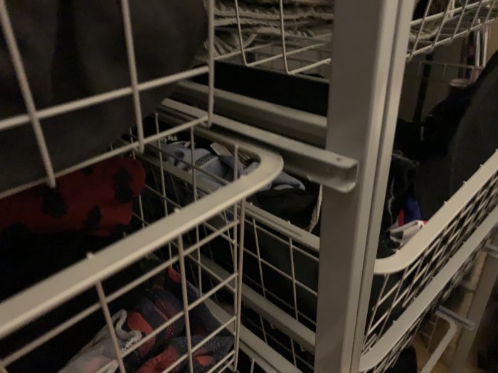 Trådbackar med kläder på glidskenor i en walk-in closet.