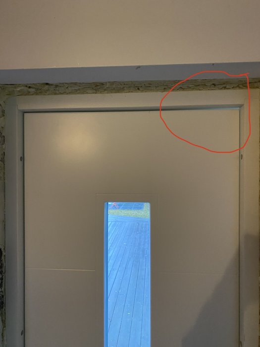Nyinstallerad vit ytterdörr sett inifrån med en markerad buktning i överkanten på handtagssidan.