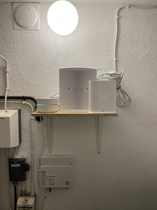 Enkel hemmanätverksuppsättning på hylla med router, Google WiFi-puckar och Arlo box, ovanför elutrustning.