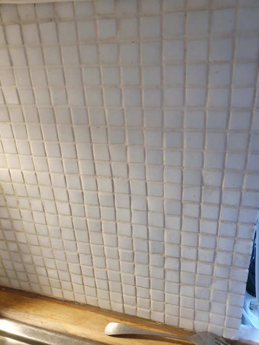 Vit mosaik kakelvägg över köksbänk som potentiell yta för att sätta upp skurna klinkerplattor.