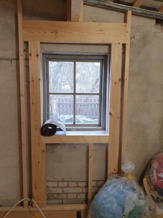 Nyinstallerat fönster i trästomme inomhus under renovering med synligt verktyg och isoleringsmaterial.