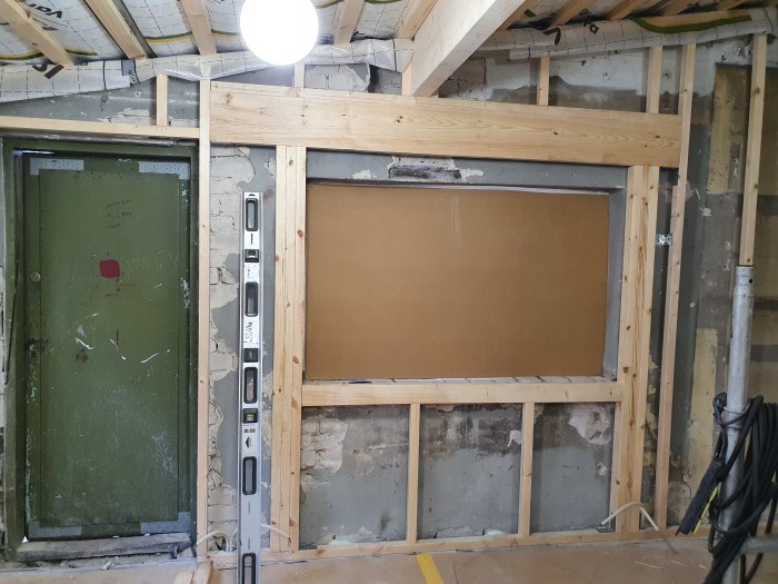 Renoveringsarbete med synlig trästomme, isolering och gammal dörr i ett pågående byggprojekt.