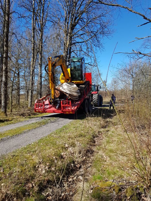 Grävmaskin på släpvagn bredvid skogsväg, i förberedelse för bergvärmeinstallation.