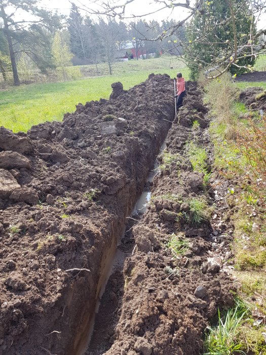 Grävd schakt för bergvärmeinstallation med person som inspekterar arbetet på landet.