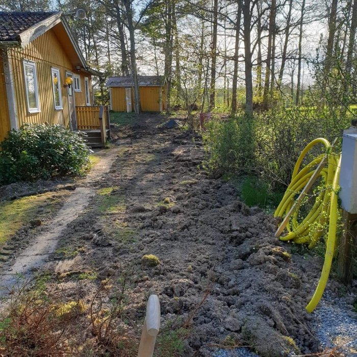 Grävd trädgård vid gult hus i förberedelse för bergvärme med gula rör på marken.