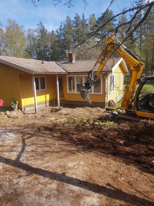 Grävmaskin framför hus med borttagen veranda inför utbyggnad.