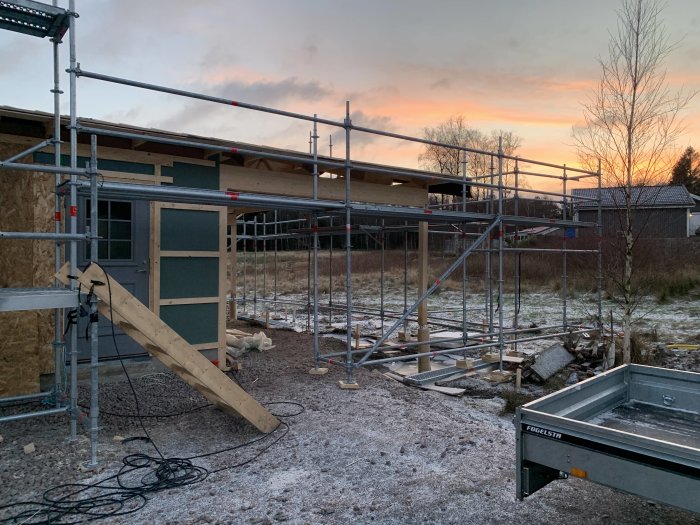 Ett garage under uppbyggnad med ställningar runtom och en nyligen installerad ytterdörr, i skymningen.