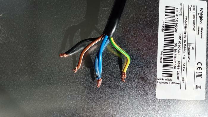 Elkabel med brun, blå, gulgrön och svart tråd från induktionshäll, oisolerade ändar, mot grå bakgrund.