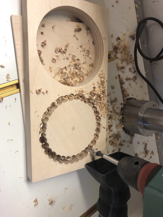 Arbetsprocess med plywood där hål skapas med cylinderborr, omgiven av spån och en borr.