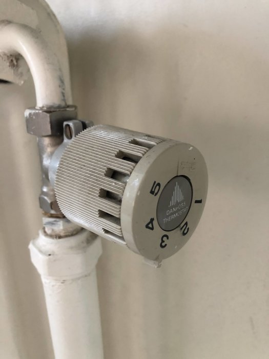 Slitet termostatventilhuvud märkt "Danfoss" på en vit radiator, indikerar behov av utbyte.