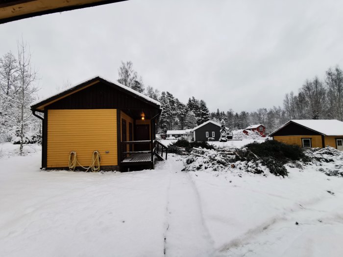 Ett gult hus med ett avverkat trädparti täckt av snö i förgrunden, vilket ger mer utrymme på tomten.