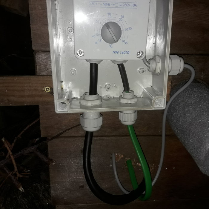 Elektrisk kopplingsdosa med justerbar termostat och flera kabelgenomföringar monterad på en trävägg.