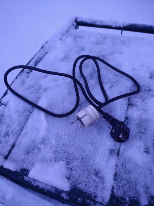 Elektrisk kabel med stickpropp på snötäckt yta, koppling för kupévärmaruttag.