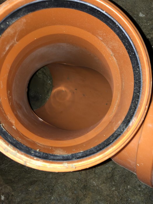 Närbild på en Fernco-koppling som förbinder ett orange plastavloppsrör med ett betongrör.