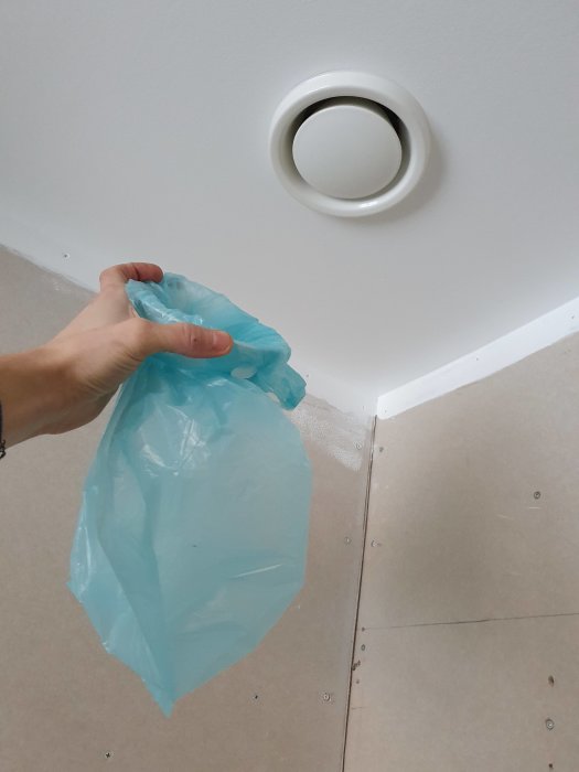 Hand håller en uppblåst plastpåse under en vit ventil i taket för att mäta frånluftsflöde.