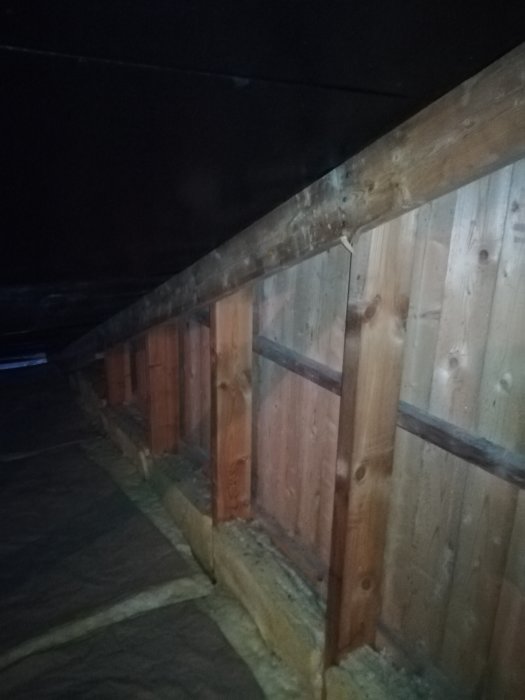 Vindutrymme med träreglar och isolering, svarta prickar synliga på väggen, indikerar potentiell mögelbildning.