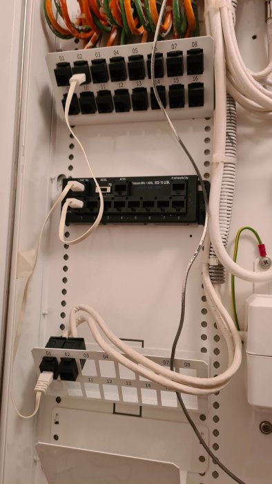 Ett öppet mediaskåp med patchpanel och nätverkskablar, märkta utsatta portar som ska kopplas för internet.