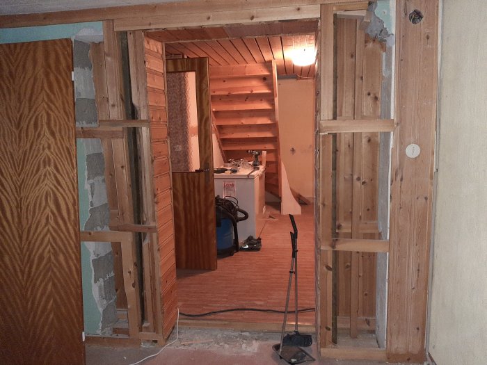 Delvis rivet väggparti i källare med träreglar och en stöttande träpelare, förberedelse för murararbete.