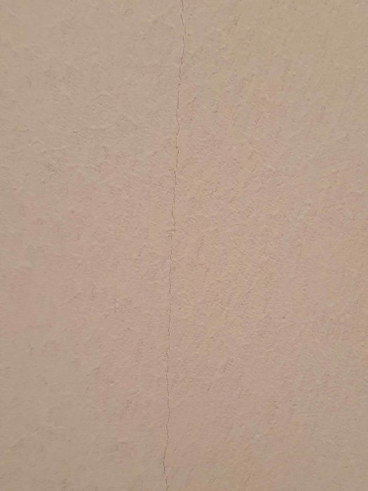 Nymålad rosa vägg med en synlig vertikal spricka som sträcker sig uppåt.