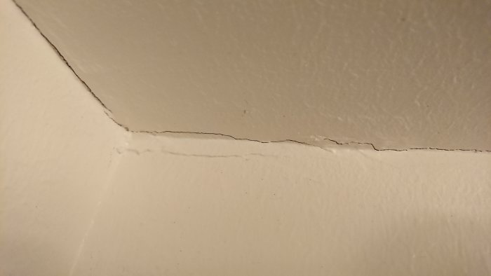 Sprickor i målat badrumstak nära hörnet, med indikation på flerskiktskonstruktion.